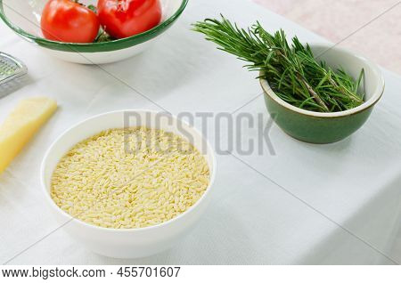 Raw Risoni In A White Bowl With Ingredients For Making Pasta On A Light Background. The Concept Of T