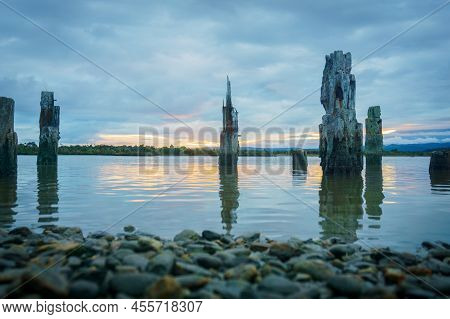 Lagoon At Okarito With Old Wharf Posts At Sunset With Overcast Sky