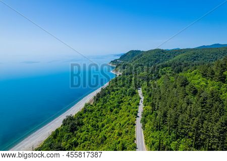 Asphalt Road Is Meandering Between Blue Sea And Green Mountains. Aerial View Of Car Driving Along Th