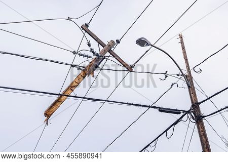 Low Angle View Of A Severed Wooden Utility Pole, Tangled With Overhead Electric Supply Wires In The 