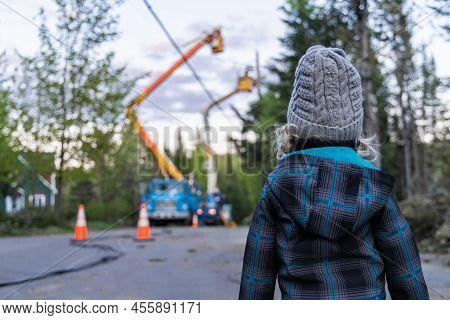 Rear View Of A Curious Four Year Old Boy Standing Outside As Powerline Engineers Are Seen Blurry In 