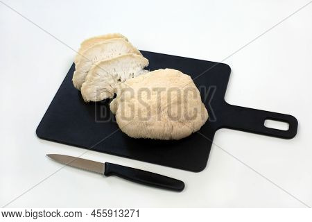 Pieces Of White Lions Mane Mushroom On Black Cutting Board And Knife On White Background
