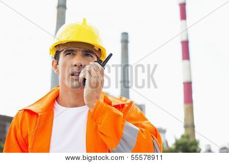 Male construction worker wearing reflective workwear communicating on two way radio at site