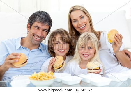Glückliche Familie essen Hamburger, die auf dem Boden sitzend