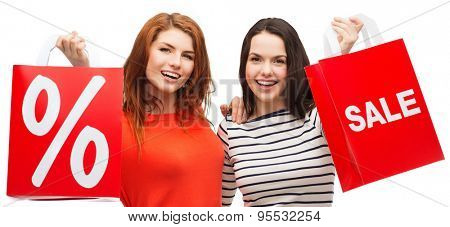 shopping, sale, and gift sconcept - two smiling teenage girls with shopping bags and percent sign