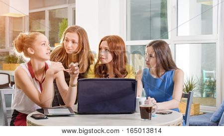 Group of four pretty businesswomen working togeather with new startup project using laptop computer in modern loft. People and teamwork concept - happy creative team in office. Casually dressed female colleagues talking in a meeting room.