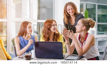 Group of four pretty businesswomen working togeather with new startup project using laptop computer in modern loft. People and teamwork concept - happy creative team in office. Casually dressed female colleagues talking in a meeting room.