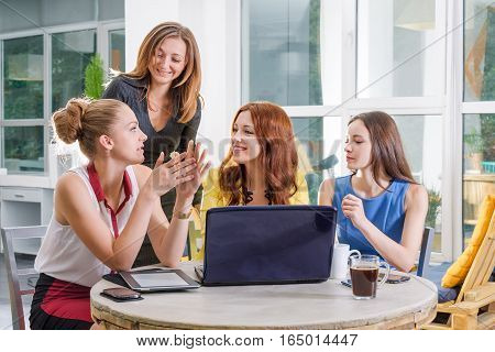 Group of four pretty businesswomen working togeather with new startup project using laptop computer in modern loft. People and teamwork concept - happy creative team in office. Casually dressed female colleagues talking in a meeting room.