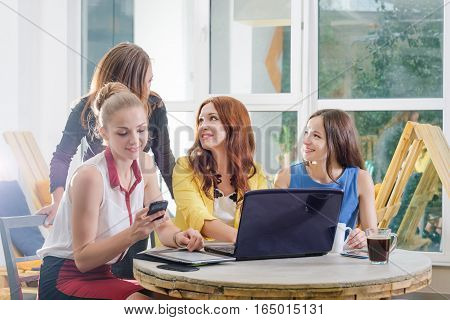 Group of four pretty businesswomen working togeather with new startup project using laptop computer in modern loft. People and teamwork concept - happy creative team in office. Casually dressed female colleagues talking in a meeting room.