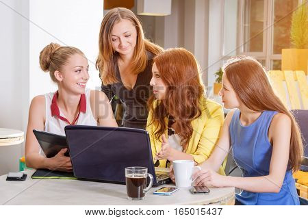 Group of four pretty businesswomen working togeather with new startup project using laptop computer in modern loft. People and teamwork concept - happy creative team in office. Casually dressed female colleagues talking in a meeting room.
