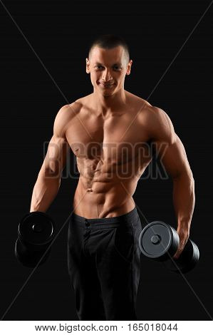 Tuned body. Studio portrait of a young handsome fitness man posing with a dumbbell showing off his stunning muscled torso on dark background