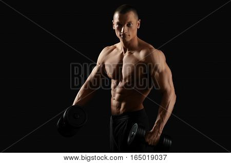 In the name of perfect body. Horizontal studio shot of a young bodybuilder man posing with dumbbells smiling to the camera posing shirtless with his fit and toned torso