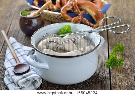 Hot Bavarian white sausages in an enamel cooking pot served on a wooden table with fresh pretzels and sweet mustard