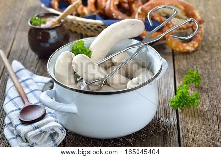 Hot Bavarian white sausages in an enamel cooking pot served on a wooden table with fresh pretzels and sweet mustard