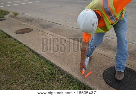 Man in safety gear spray painting numbers on a sidewalk while surveying.