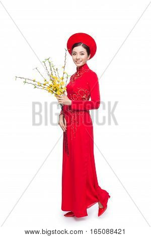 Full length of a beautiful Asian woman on traditional festival costume Ao Dai holding Hoa Mai tree (Ochna Integerrima) flower. Tet holiday. Lunar New Year.
