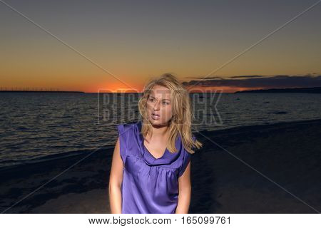 Beautiful girl in a bright violet dress by the sea. Against the background of the summer lanshaft. Young romantic woman in the sunshine, sunset.