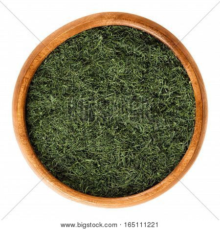 Dried dill fronds in wooden bowl, also called dill weed. Shredded green leaves of Anethum graveolens, used as herb and spice. Isolated macro food photo close up from above on white background.
