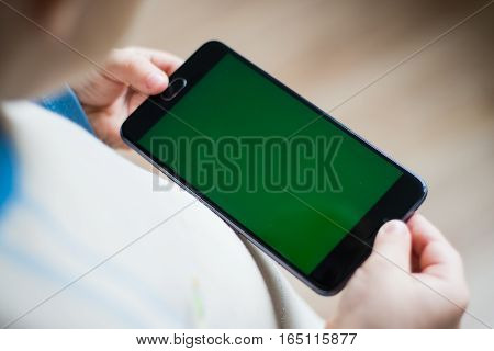 The child is holding a phone in his hand with a green screen for chroma keyer