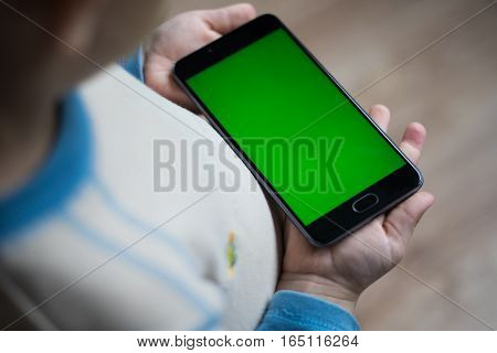 The child is holding a phone in his hand with a green screen for chroma keyer