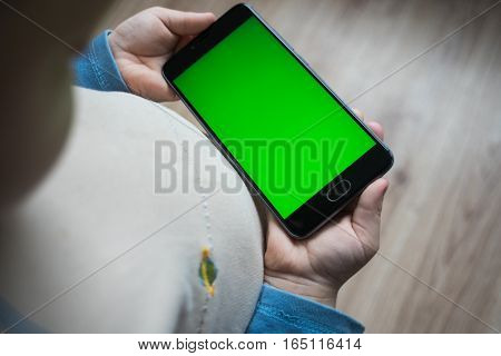 The child is holding a phone in his hand with a green screen for chroma keyer