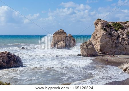 Aphrodite's Rock, Cyprus, shot in late summer and shows large waves crashing onto the large rocks. A few people on the beach show the scale of the rocks.