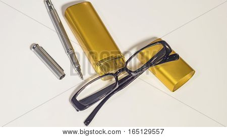 Black glasses, gold case and pen on the isolate white background
