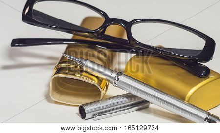 The glasses, gold case and a pen. White isolate background. Closeup.