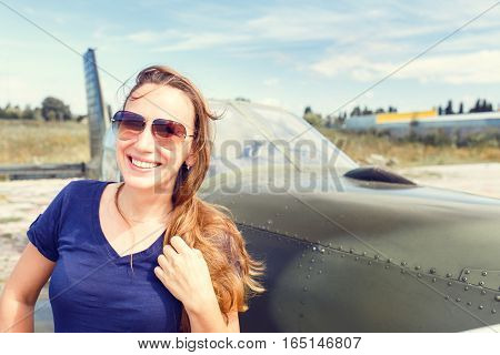 Young happy woman standing near sport plane on airfield delighted before flight.