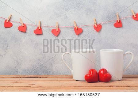 Valentines day concept with white coffee cups and heart shapes over rustic background with garland