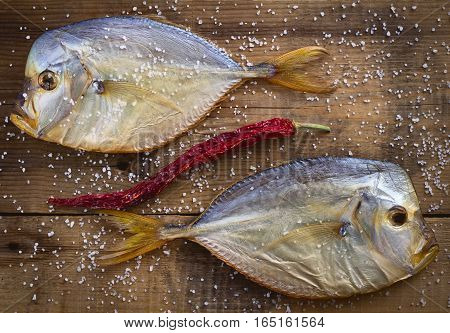 Two smoked Vomero on a wooden background. Sprinkle with salt. Curved red pepper pod. Top view