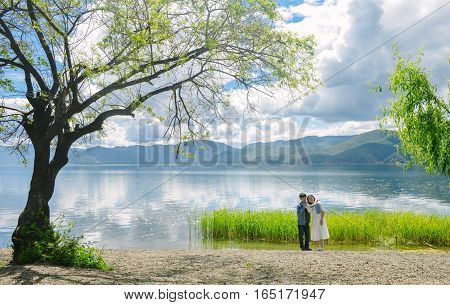 Young Chinese couple stand hand in hand on the bank of Lugu lake, smiling,  at Daluoshui village, Lijiang, China