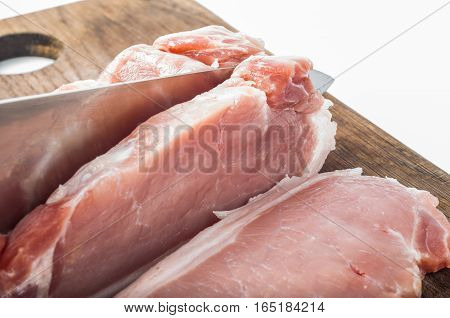 Cutting raw meat on wooden board by hand with metal knife