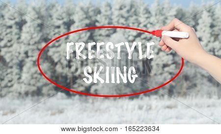 Woman Hand Writing Freestyle Skiing With Marker Over Winter Forest.