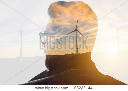 Double exposure portrait of a businessman thinking about renewable electricity combinated with sunset landscape and winmills