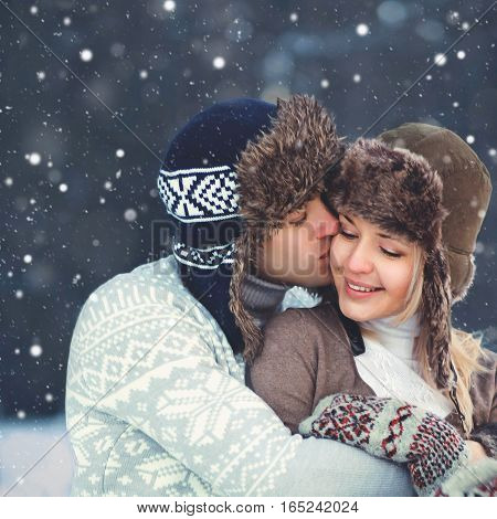 Portrait happy young couple in love at winter day man gentle kissing woman wearing hat knitted sweater tenderness moment over snowflakes