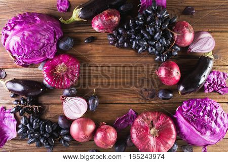Purple fruits and vegetables. Blue onion purple cabbage eggplant grapes and plums on a wooden background.