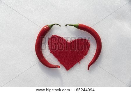 Hot chili love in the snow. Two red peppers and a textile heart