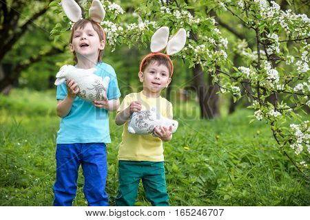 Two Little Kids Boys And Friends In Easter Bunny Ears During Traditional Egg Hunt In Spring Garden,