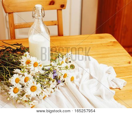Simply stylish wooden kitchen with bottle of milk and glass on table, summer flowers camomile, healthy foog moring concept noone