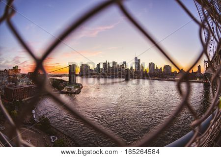 Brooklyn bridge and downtown skyline in New York. Manhattan skyscrapers seen through a fence on Manhattan bridge at dusk. Travel and architecture concepts