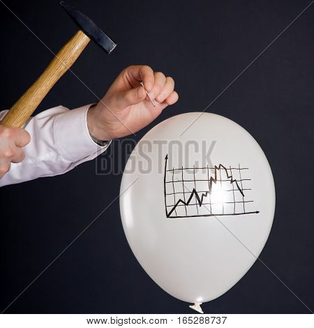 businessman hitting a nail into a white balloon with a decaying financial chart