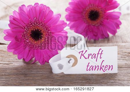Label With German Text Kraft Tanken Means Relax. Pink Spring Gerbera Blossom. Vintage, Rutic Or Aged Wooden Background. Card For Spring Greetings.
