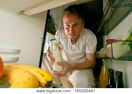a young man is taking a bottle of milk from hsi fridge