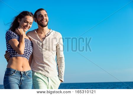 Couple walking on beach. Young happy interracial couple walking on beach smiling holding around each other. Latino woman, Caucasian man.