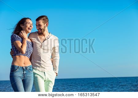 Couple walking on beach. Young happy interracial couple walking on beach smiling holding around each other. Latino woman, Caucasian man.