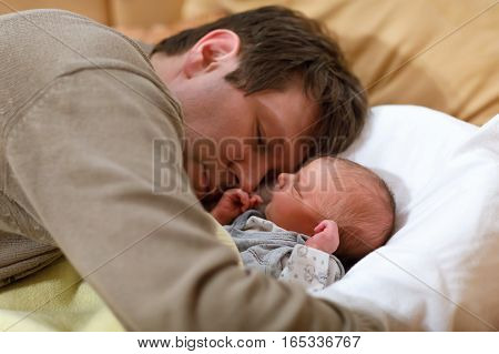 Middle aged father giving kiss his newborn baby daughter. Young dad hugging and cuddling with baby girl at home. Happy parenthood, carefree childhood, family, love. Cute adorable baby sleeping