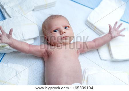 Cute adorable newborn baby on changing table with diapers. Cute little girl or boy looking at the camera. Dry and healthy body and skin concept. Baby nursery