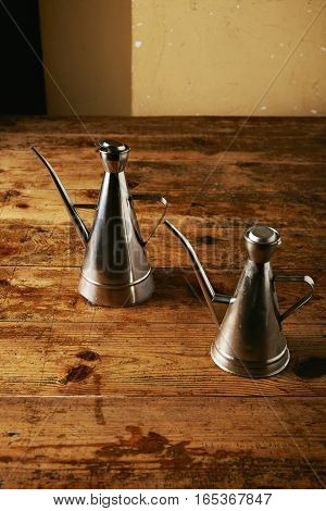 Two similar shaped steel olive oil cruets in a rustic vintage beige toned kitchen