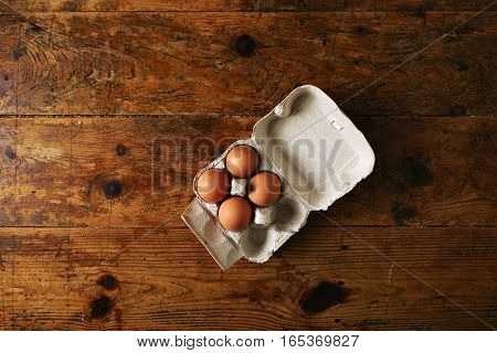 Opened recyclable egg carton for six eggs containing four big brown eggs on a rough rustic brown wooden table